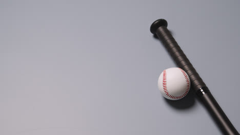 Overhead-Baseball-Still-Life-With-Person-Picking-Up-Bat-And-Ball-Against-Grey-Background